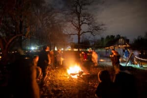 Families stand around a bonfire, preparing to toss a green sprig on the yule log.